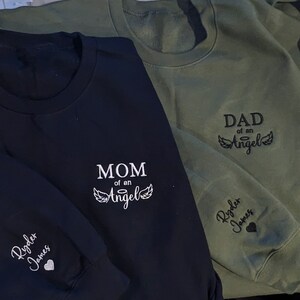 Custom embroidered “Mom Dad of an Angel” sweatshirt with child’s name and heart on sleeve — personalized memorial gift for mom, dad, or grandparent, perfect Christmas remembrance hoodie or crewneck.