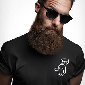 May include: Black t-shirt featuring a white cartoon ghost with the word "boo" in a speech bubble. The ghost has a simple design with dots for eyes and a wavy bottom. The shirt is worn by a person with a beard.