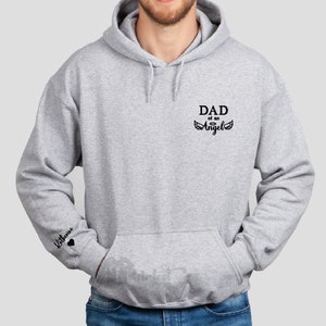 May include: A gray hooded sweatshirt with the text "DAD of an Angel" and wings on the front. The left sleeve has the text "Liliana" with a heart.