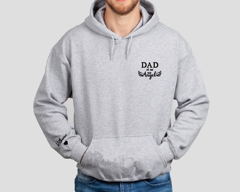 May include: A gray hooded sweatshirt with the text "DAD of an Angel" and wings on the front. The left sleeve has the text "Liliana" with a heart.