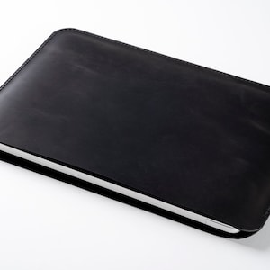 May include: A black leather laptop sleeve with a subtle texture. The sleeve is closed and lying flat on a white surface.
