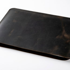 May include: A dark brown leather laptop sleeve with a stitched edge.
