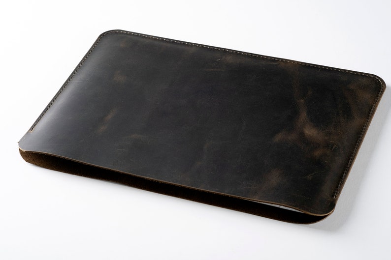 May include: A dark brown leather laptop sleeve with a stitched edge.