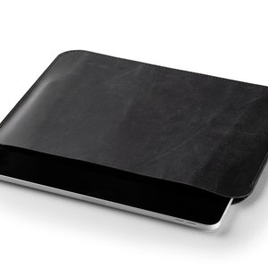 May include: A black leather tablet sleeve with a tablet partially inserted. The sleeve has a rectangular shape with rounded corners and a textured surface. The tablet has a silver frame and a black screen.