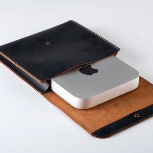 Puede incluir: Una funda de cuero negro con forro de cuero marrón, diseñada para contener una pequeña computadora plateada con un logotipo de Apple.