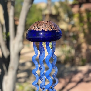Peut inclure: Un carillon en verre en forme de méduse bleue avec un sommet de couleur cuivre et de longues tentacules en spirale.