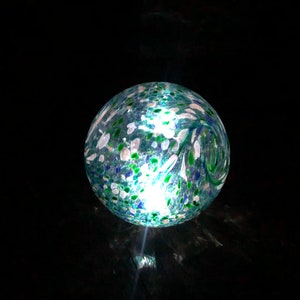 May include: A blue glass globe with white and green flecks. The globe is illuminated from within, creating a warm glow.