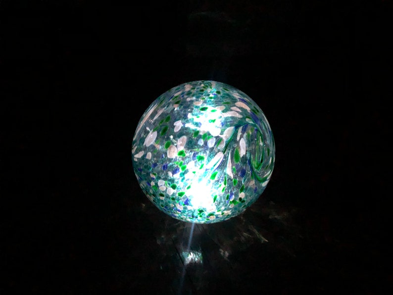 May include: A blue glass globe with white and green flecks. The globe is illuminated from within, creating a warm glow.