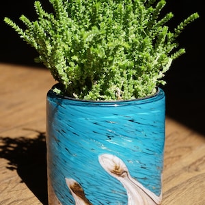 May include: A teal blue glass planter with a white and brown swirl design. A green succulent plant is growing in the planter.