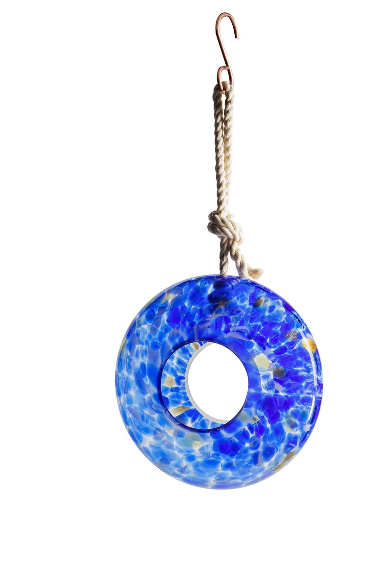 May include: A blue glass bird feeder shaped like a ring with a rope and hook for hanging. The glass is speckled with white and gold.