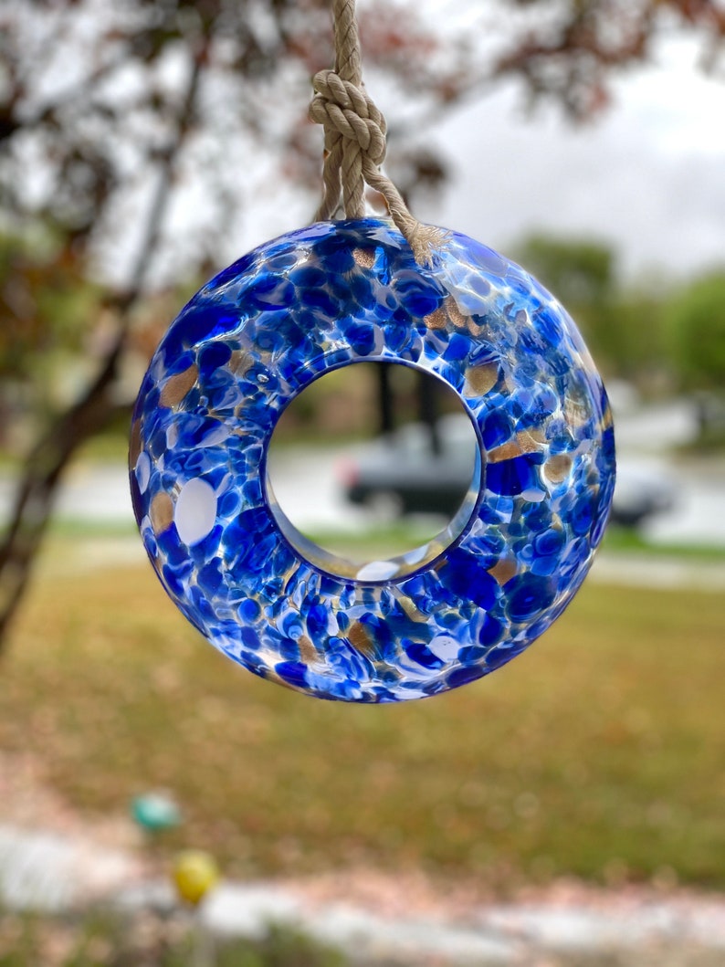May include: A blue glass ring with gold and white flecks, hanging from a natural twine cord. The ring has a large hole in the center.