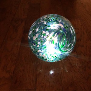 May include: A round, clear glass globe with a swirling pattern of green, blue, and white. The globe is lit from within, creating a warm glow.
