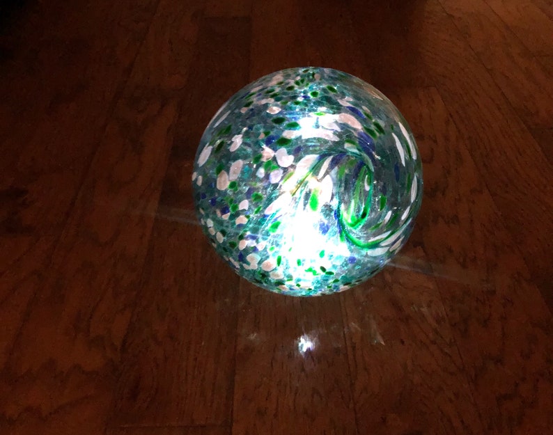 May include: A round, clear glass globe with a swirling pattern of green, blue, and white. The globe is lit from within, creating a warm glow.