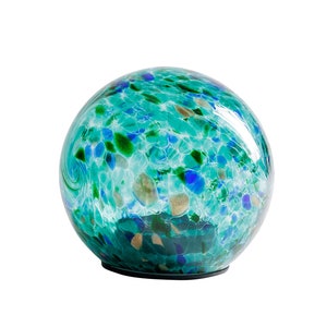 May include: A round glass globe with a swirling pattern of blue, green, and white. The globe is sitting on a black base.