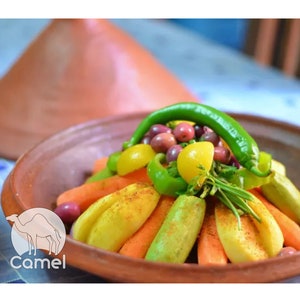 May include: A traditional Moroccan tagine dish with a colorful arrangement of vegetables, including carrots, zucchini, peppers, and olives. The vegetables are arranged in a circular pattern and topped with a green chili pepper. The tagine is served in a terracotta dish with a lid.