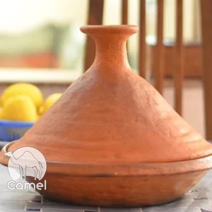 May include: A terracotta tagine, a traditional Moroccan cooking pot with a conical lid, is shown on a table. The tagine is made of unglazed clay and has a natural reddish-brown color.