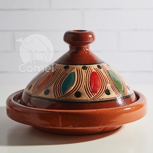 Könnte beinhalten: Eine Terrakotta-Tajine mit Deckel, verziert mit einem dekorativen Muster aus bunten Wirbeln und Punkten. Die Tajine ist ein traditioneller marokkanischer Kochtopf.