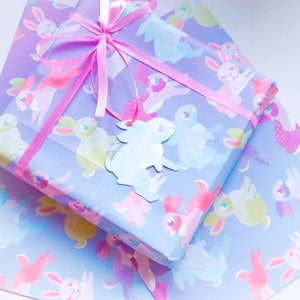 May include: A blue gift box with a pink ribbon and a white bunny tag. The box is wrapped in paper with a pattern of pastel coloured bunnies.