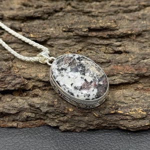 Könnte beinhalten: Ovale Anhänger Halskette mit silberfarbener Fassung und einem Stein mit einem gesprenkelten Muster aus Weiß, Schwarz und Kastanienbraun. Der Anhänger hängt an einer silbernen Kette.