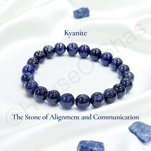 May include: A dark blue kyanite beaded bracelet. The bracelet is made of round, polished stones with a speckled appearance. The text "Kyanite" and "The Stone of Alignment and Communication" are also visible.