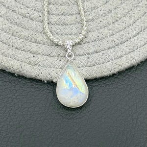 May include: A silver necklace featuring a teardrop-shaped moonstone pendant with iridescent blue and yellow flashes. The pendant is set in a simple silver bezel and hangs from a textured silver chain with a woven, rope-like appearance.