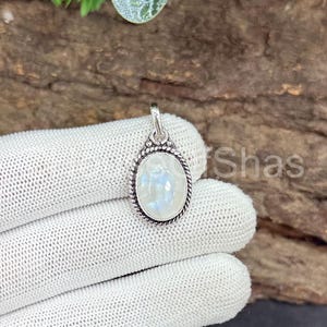 May include: Oval-shaped moonstone pendant with a silver-colored setting. The moonstone has a pearly, iridescent appearance. The pendant is suspended from a small loop at the top. The setting has a rope-like border.