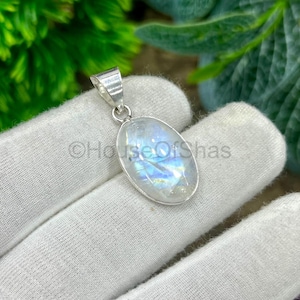 May include: Oval moonstone pendant with a silver bail. The moonstone has a shimmering, iridescent quality, with blue and white hues. The pendant is set against a white background, with the text "HouseOfShas". A piece of jewellery.