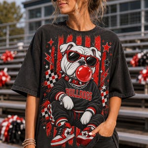 May include: A black short-sleeve t-shirt featuring a graphic of a bulldog wearing red sunglasses and a spiked collar, blowing a red bubble. The bulldog wears a black sweatshirt with the word BULLDOGS in red, black sweatpants, and red sneakers.