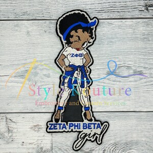 May include: Embroidered patch featuring a cartoon character wearing a white shirt with "ZPB" on it, blue jeans, and a blue bandana. The character has brown skin, black hair, and blue eyes. The patch also includes the text "Zeta Phi Beta girl".