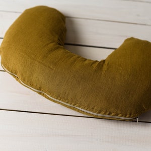 May include: A mustard yellow U-shaped pillow with a white zipper. The pillow is made of a soft, textured fabric.