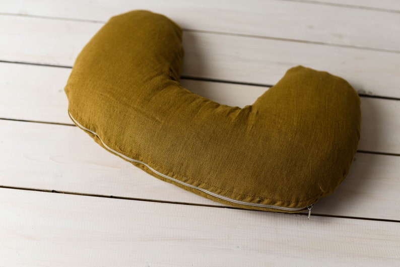 May include: A mustard yellow U-shaped pillow with a white zipper. The pillow is made of a soft, textured fabric.