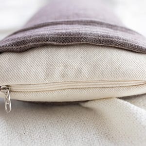 May include: A white pillow with a zipper closure and a brown linen cover folded over the top.