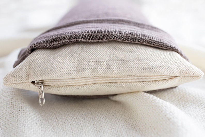 May include: A white pillow with a zipper closure and a brown linen cover folded over the top.
