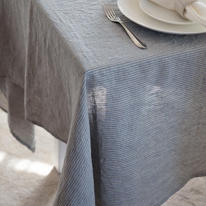 May include: A gray and white striped linen tablecloth draped over a table. A white plate, napkin, and fork are set on the table. The tablecloth has a textured appearance.