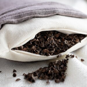 May include: A white pillowcase with a zipper is filled with buckwheat hulls. The pillowcase is open and the hulls are spilling out onto a white surface.