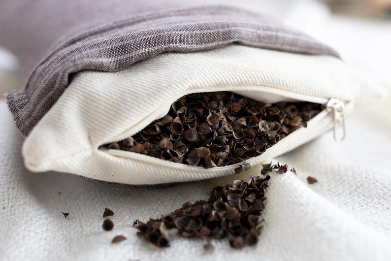 May include: A white pillowcase with a zipper is filled with buckwheat hulls. The pillowcase is open and the hulls are spilling out onto a white surface.