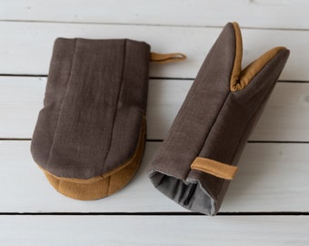 May include: Two brown oven mitts with tan trim. One mitt is a potholder style and the other is a full hand mitt.