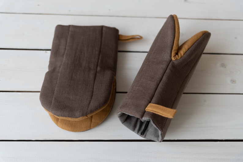 May include: Two brown oven mitts with tan trim. One mitt is a potholder style and the other is a full hand mitt.