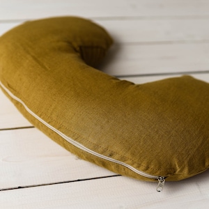 May include: A mustard yellow crescent-shaped pillow with a white zipper.