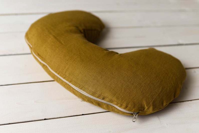 May include: A mustard yellow crescent-shaped pillow with a white zipper.