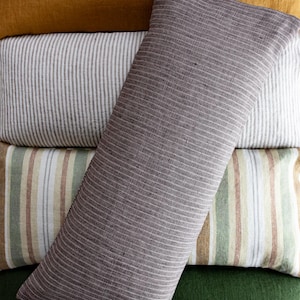 May include: A stack of four decorative pillows with different striped patterns. The top pillow is a dark gray with thin white stripes, the second pillow is white with thin gray stripes, the third pillow is a light brown with thin white and green stripes, and the bottom pillow is a solid dark green.