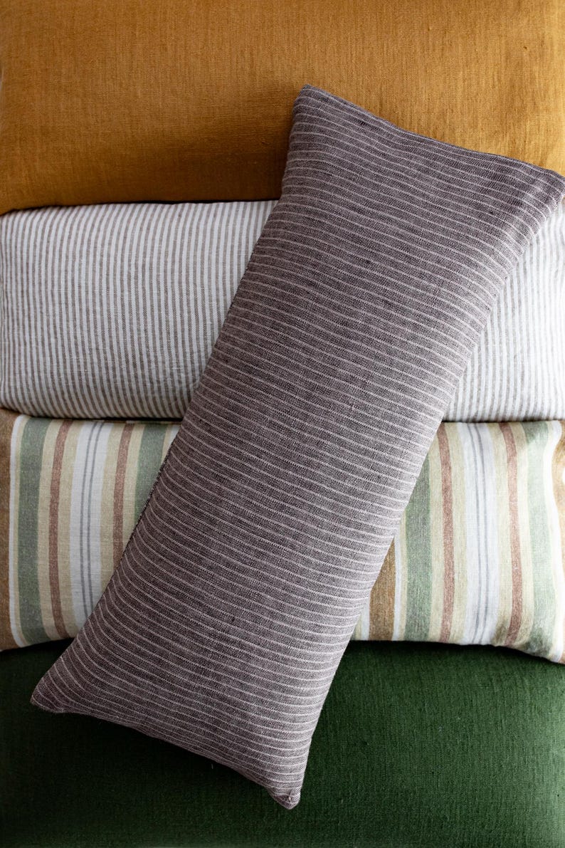 May include: A stack of four decorative pillows with different striped patterns. The top pillow is a dark gray with thin white stripes, the second pillow is white with thin gray stripes, the third pillow is a light brown with thin white and green stripes, and the bottom pillow is a solid dark green.