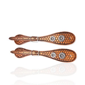 May include: A pair of brown leather spur straps with silver floral accents. The straps have a star-shaped pattern and are designed for cowboy boots.