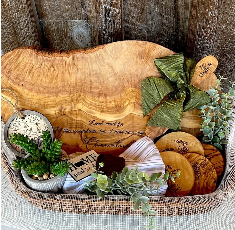 Puede incluir: Una bandeja de servir de madera con un acabado de grano de madera natural. La bandeja est&aacute; llena de una variedad de art&iacute;culos, incluyendo una peque&ntilde;a suculenta en maceta, un lazo verde, un letrero de madera que dice "Home Sweet Home" y varios posavasos de madera peque&ntilde;os con dise&ntilde;os grabados. La bandeja est&aacute; sentada sobre una superficie tejida.