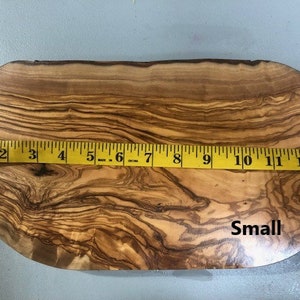 Puede incluir: Una tabla de cortar de madera de olivo peque&ntilde;a, de forma ovalada, con un patr&oacute;n de veta de madera natural. La tabla mide 13 pulgadas de largo y 10 pulgadas de ancho en su punto m&aacute;s ancho. La tabla est&aacute; etiquetada como "Small".