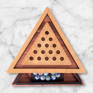 May include: A wooden triangular game board with a decorative design and circular holes. The board has a drawer containing marbles with blue, white, and gray swirls. The game board is made of light and dark brown wood.