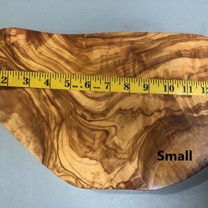 Puede incluir: Una peque&ntilde;a tabla de servir de madera natural con una forma org&aacute;nica &uacute;nica. La tabla est&aacute; hecha de madera de olivo y tiene un color marr&oacute;n intenso con un patr&oacute;n de veta natural. La tabla mide aproximadamente 33 cm de largo y tiene la palabra "Small" escrita en ella.