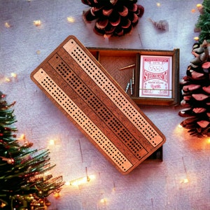 Può includere: Una tavola da cribbage rettangolare in legno con finitura marrone scuro e tre piste parallele di fori praticati. La tavola è parzialmente aperta, rivelando un vano portaoggetti contenente un mazzo di carte da gioco e diversi pioli metallici.