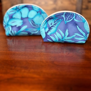 May include: Two blue and white floral print zippered pouches. The pouches are half-circle shaped and have a white zipper.