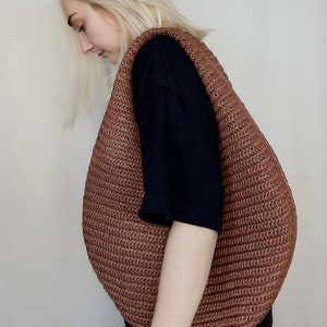 May include: A large, crescent-shaped hobo bag crafted from a brown, textured, woven material. The bag features a wide, integrated shoulder strap and a continuous, ribbed pattern throughout its surface, creating a rounded, voluminous silhouette.
